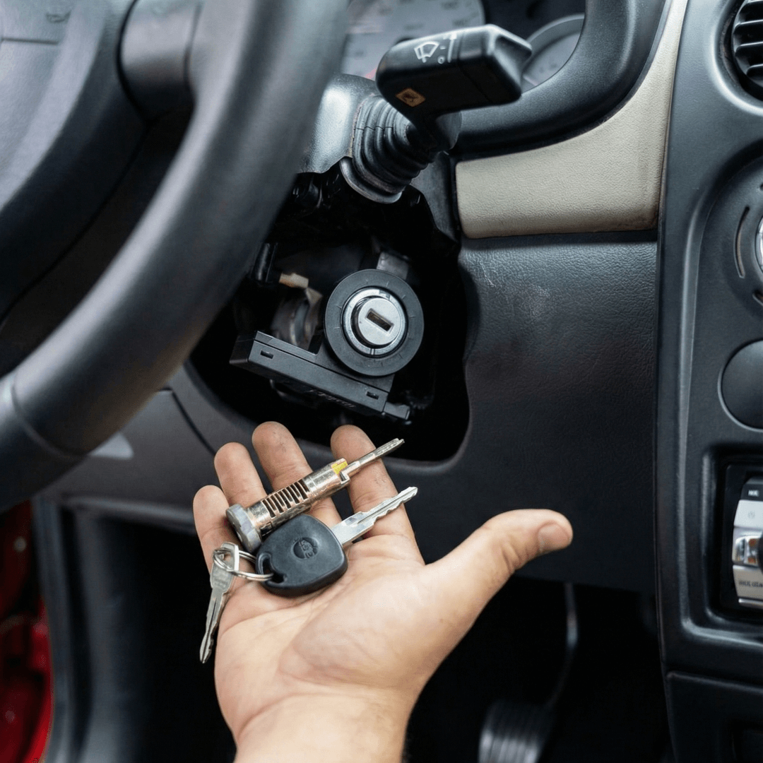 Cerrajero profesional sosteniendo llaves y bombín de encendido reparado frente a la columna de dirección de un vehículo